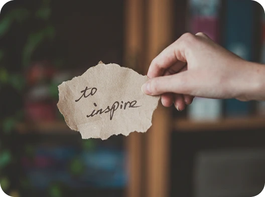 Hand holding a note reading “to inspire,” reflecting Talking Leaves Fiction’s mission to inspire writers, storytellers, and readers.