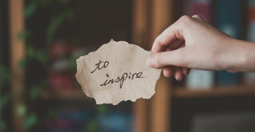 Image featuring a hand holding a note with the words “To Inspire,” symbolizing creativity and storytelling.